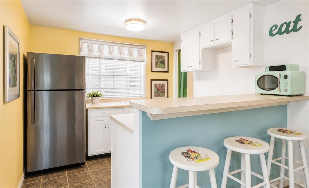 A kitchen features a stainless steel refrigerator, white cabinets, a breakfast bar, and bar stools — 526 5TH AVENUE N, SAFETY HARBOR, FL