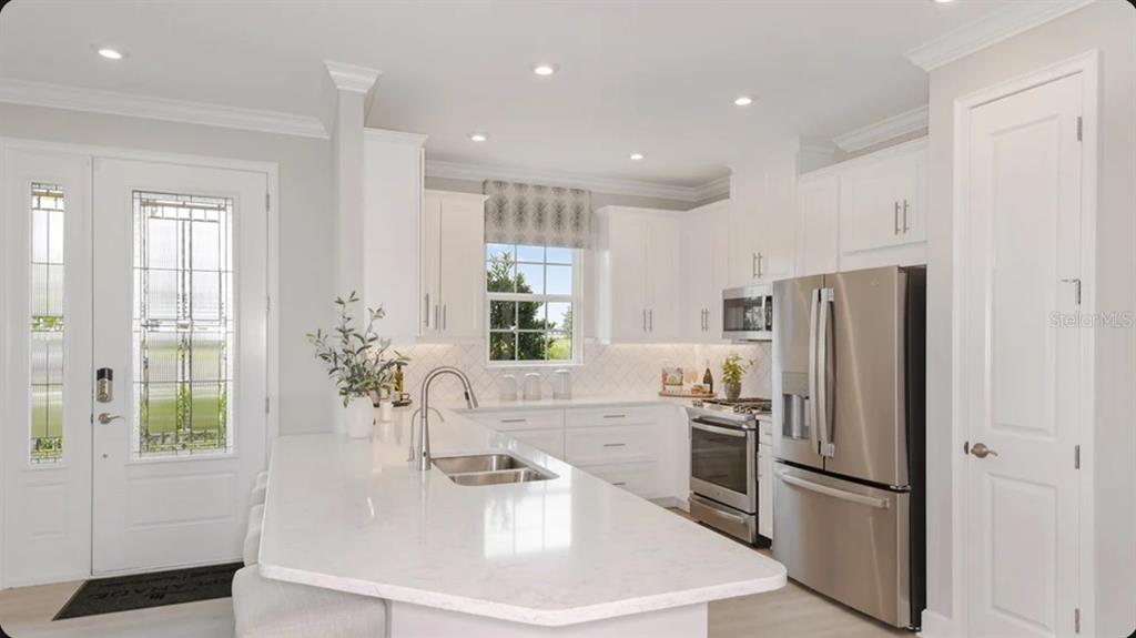 A modern kitchen features white cabinetry, stainless steel appliances, and a large quartz-topped island — 7532 MOONBEAM AVENUE, SARASOTA, FL