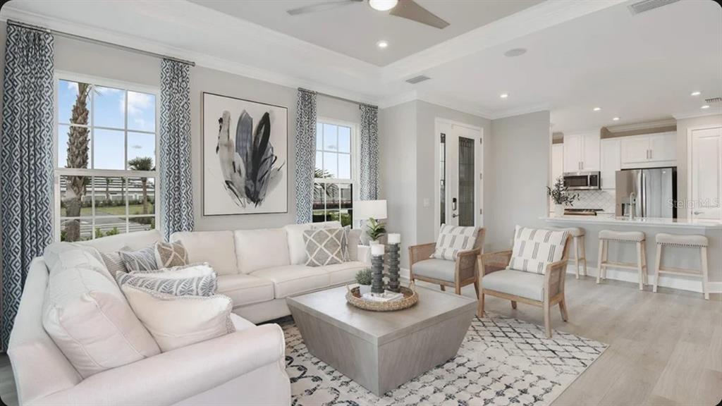 A bright living room features a white sectional sofa, a coffee table, and an open kitchen — 7532 MOONBEAM AVENUE, SARASOTA, FL