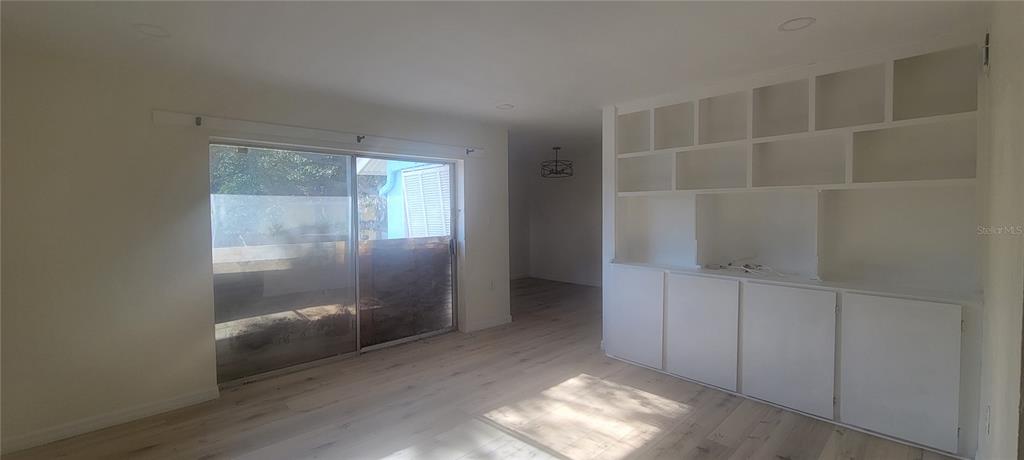 A living room features light wood-look flooring, a sliding glass door, and built-in white shelving — 3775 40TH LANE S UNIT L, ST PETERSBURG, FL