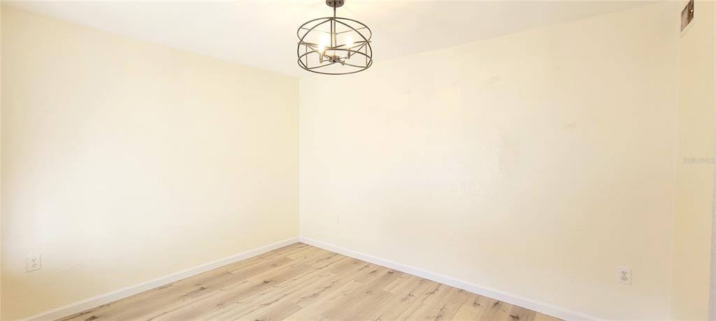 An empty room features light-colored walls, wood-look flooring, and a modern metal pendant light — 3775 40TH LANE S UNIT L, ST PETERSBURG, FL