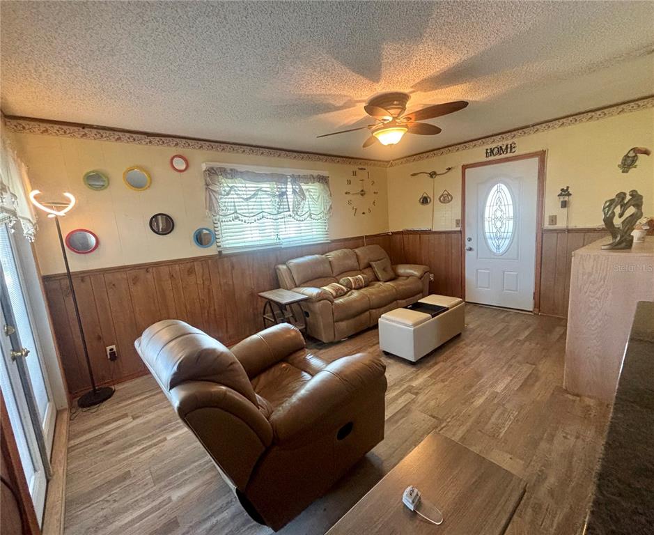 A living room features wood-paneled wainscoting, a leather sofa and recliner, and a ceiling fan — 2302 MARTHA DRIVE, LAKE ALFRED, FL