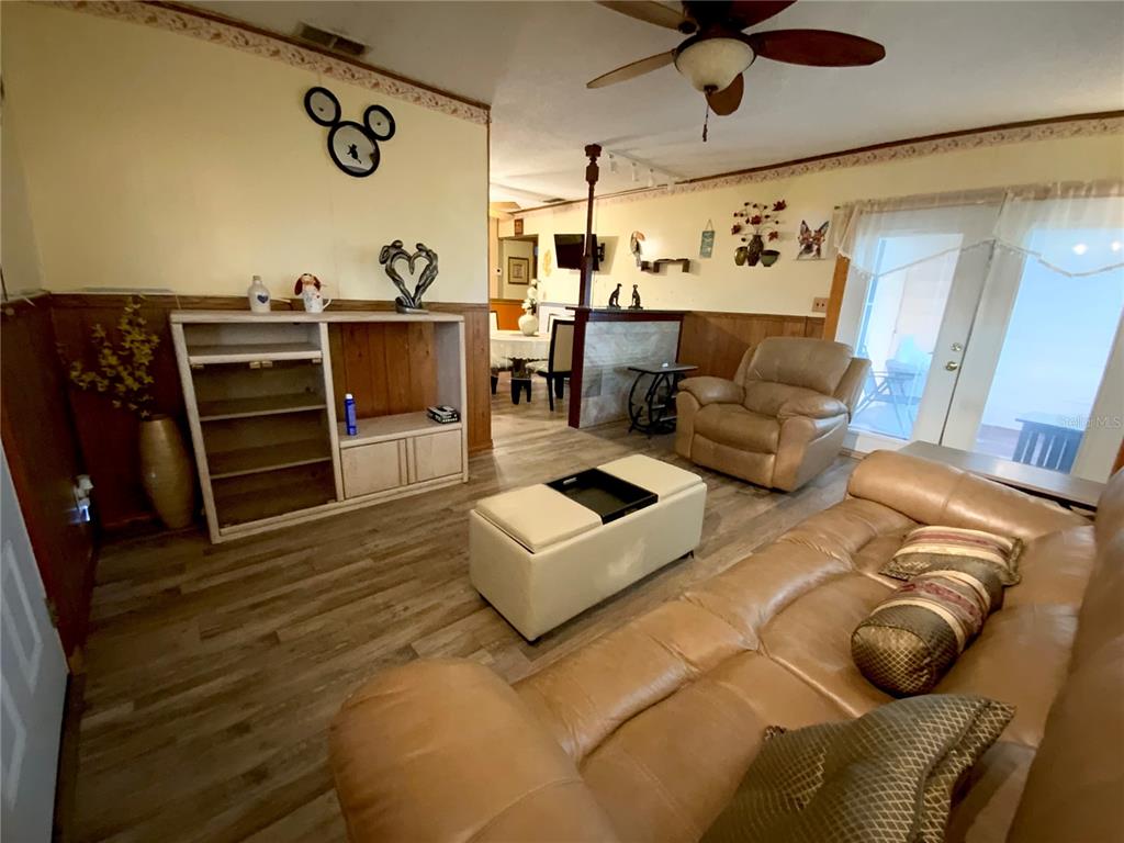 A living room features wood-look flooring, a tan leather sofa, and a central ottoman — 2302 MARTHA DRIVE, LAKE ALFRED, FL