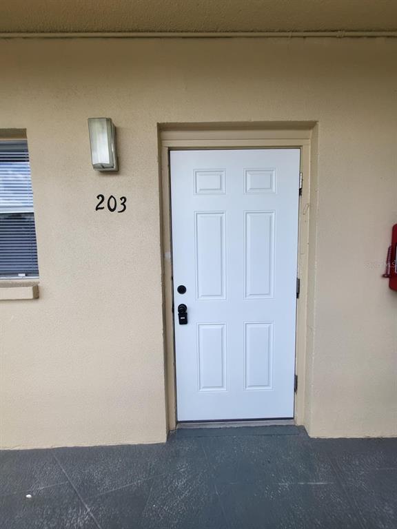 A white six-panel entry door labeled 203 is set into a beige exterior wall — 5750 80TH STREET N UNIT B203, ST PETERSBURG, FL