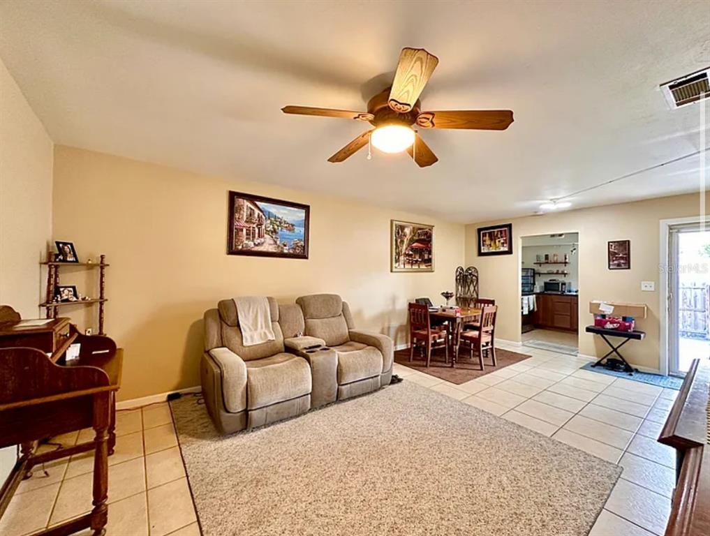 A living room with a beige sofa, ceiling fan, tile flooring, and an adjacent dining area — 712 E ARIZONA AVENUE UNIT A, DELAND, FL