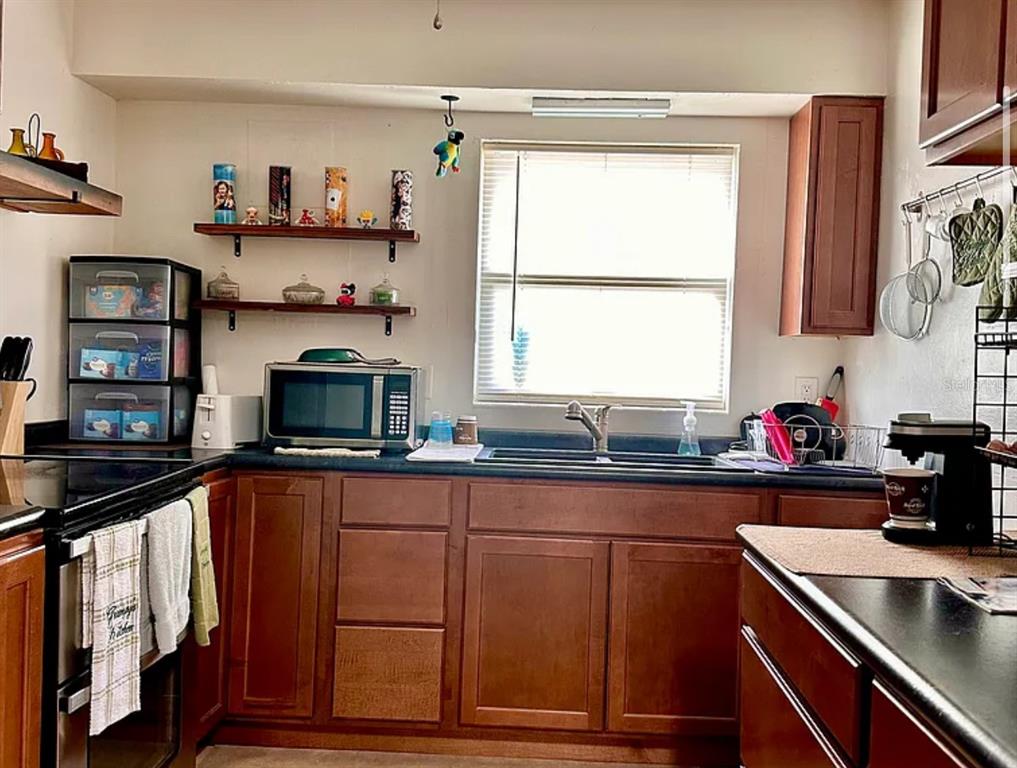 A kitchen with wooden cabinets, black countertops, a microwave, and open shelving above the sink — 712 E ARIZONA AVENUE UNIT A, DELAND, FL