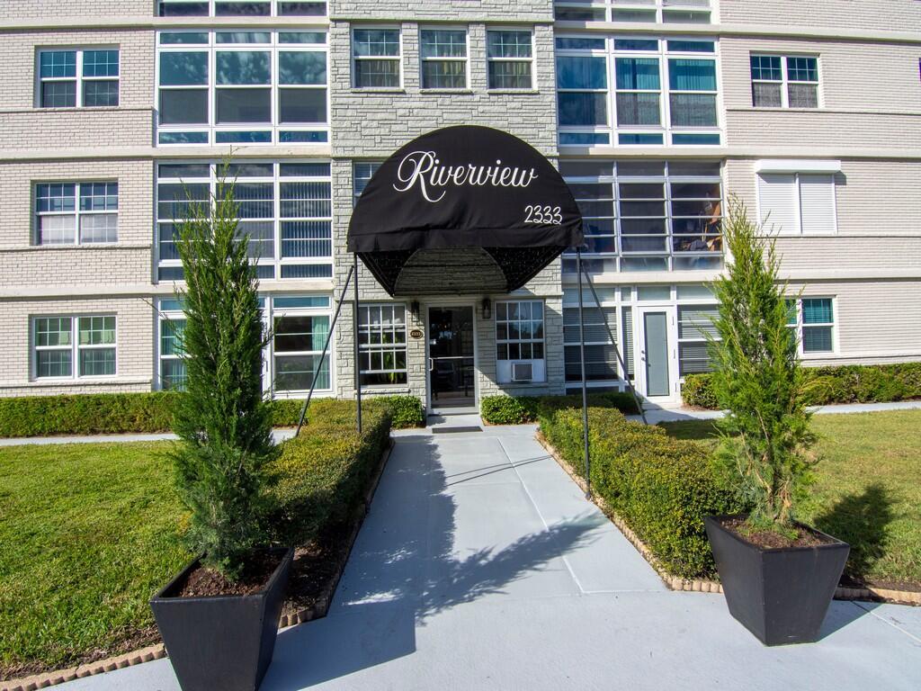 The exterior entrance of a multi-story apartment building features a black awning and walkway — 2333 Indian River Boulevard # 506, Vero Beach FL 32960, VERO BEACH, FL
