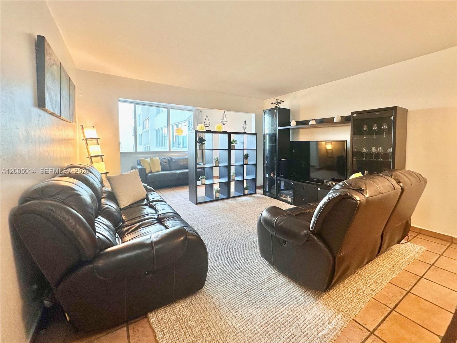 A living room features dark leather sofas, a black shelving unit, and a television console — 7135 COLLINS AVE # 811, Miami Beach FL 33141, MIAMI BEACH, FL