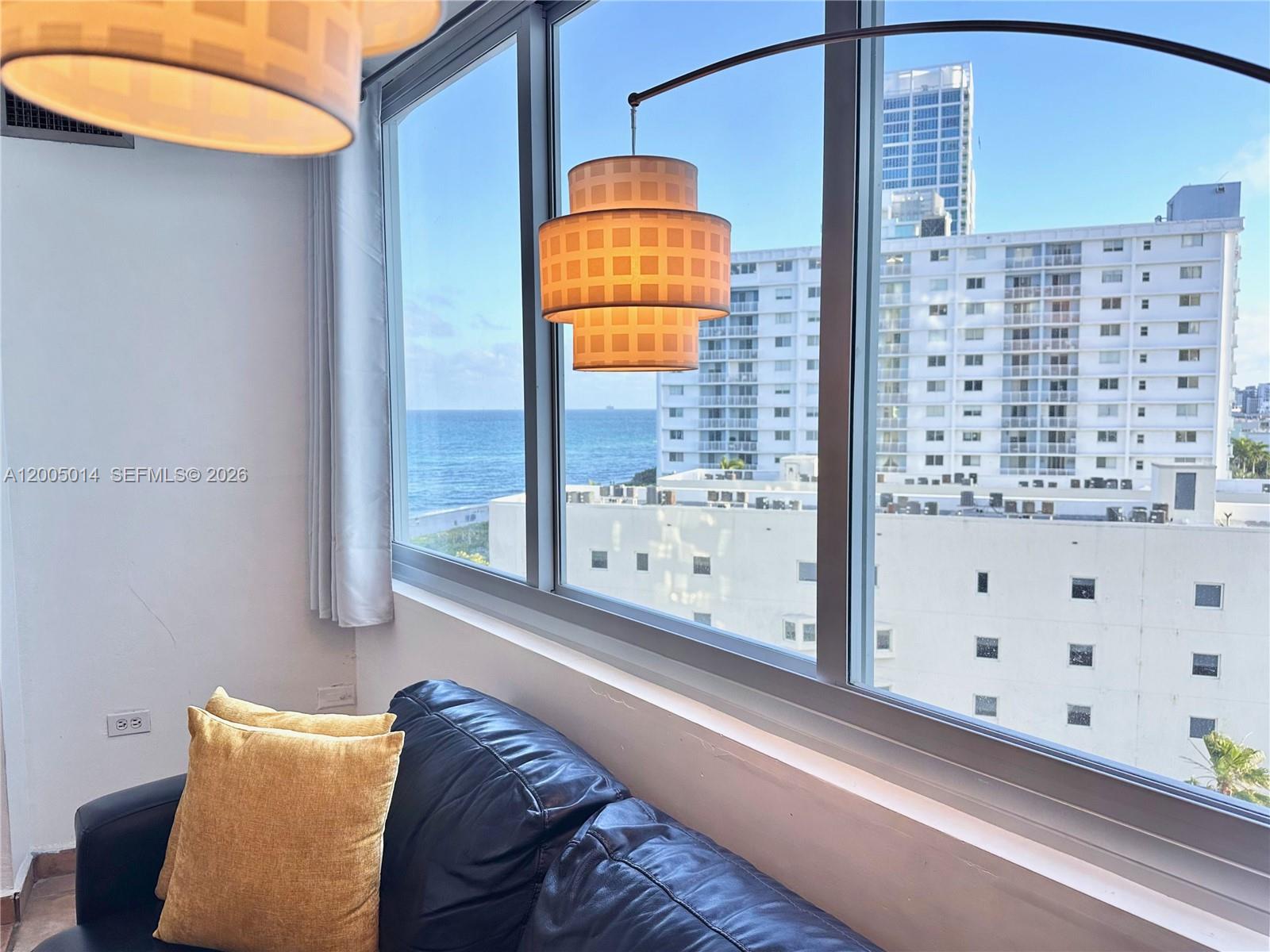A living area features a dark leather sofa, yellow pillows, and a view of the ocean — 7135 COLLINS AVE # 811, Miami Beach FL 33141, MIAMI BEACH, FL