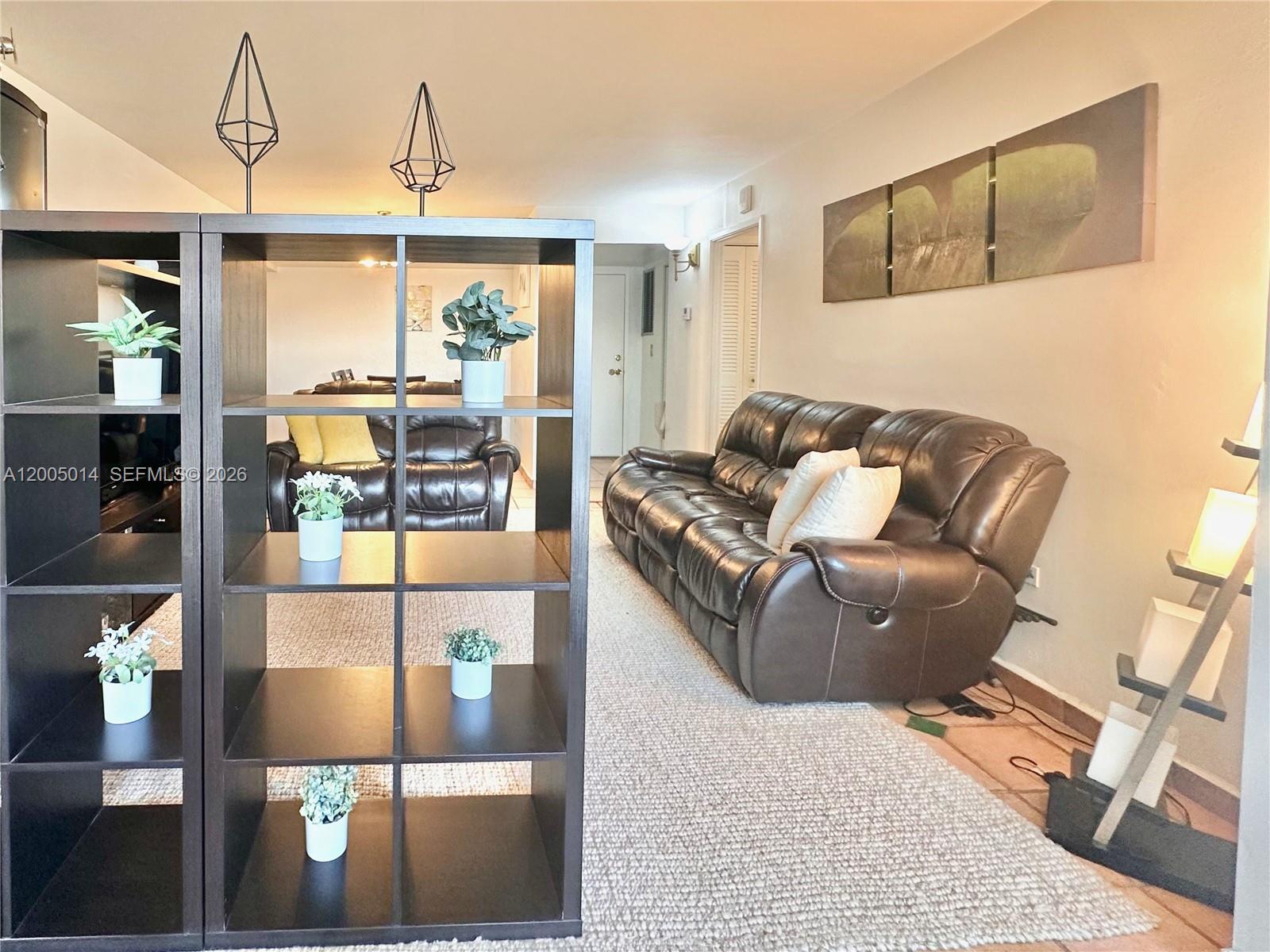 A living room features a dark brown leather sofa, a cube shelving unit, and artwork — 7135 COLLINS AVE # 811, Miami Beach FL 33141, MIAMI BEACH, FL