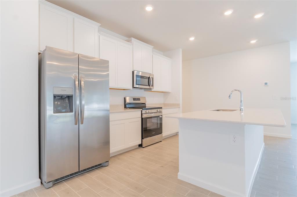 A modern kitchen features white cabinets, stainless steel appliances, and a central island with sink — 6913 SW 87TH STREET, OCALA, FL