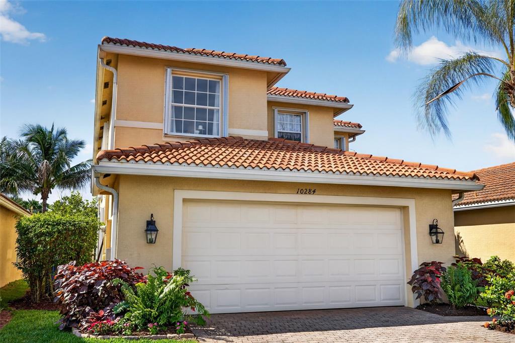 A two-story house with a beige stucco exterior, a tiled roof, and a two-car garage — 10284 CREPE JASMINE LANE, FORT MYERS, FL