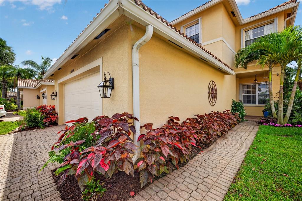 A yellow stucco house exterior features a garage, a paved walkway, and tropical landscaping — 10284 CREPE JASMINE LANE, FORT MYERS, FL