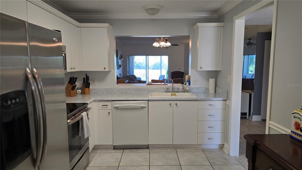 A kitchen features white cabinets, stainless steel appliances, a pass-through window, and tiled flooring — 2725 TERRA CEIA BAY BOULEVARD UNIT 102, PALMETTO, FL