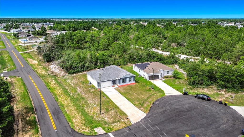 An aerial view shows two single-story houses with driveways situated near a road and forest — 106 OAK CIRCLE, POINCIANA, FL