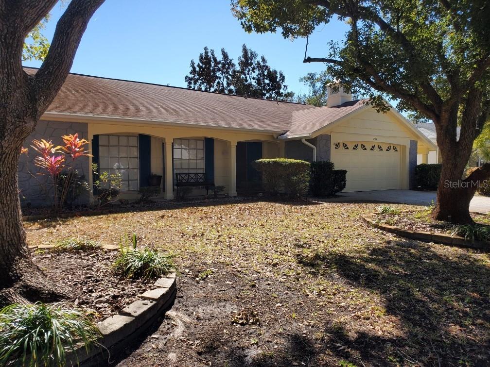 A single-story house with a beige garage, covered porch, and trees in the front yard — 8504 WAGON WHEEL LANE, HUDSON, FL