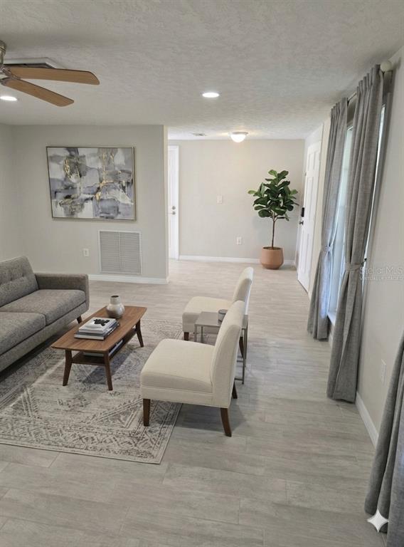 A living room features light tile flooring, a gray sofa, two accent chairs, and a plant — 8504 WAGON WHEEL LANE, HUDSON, FL