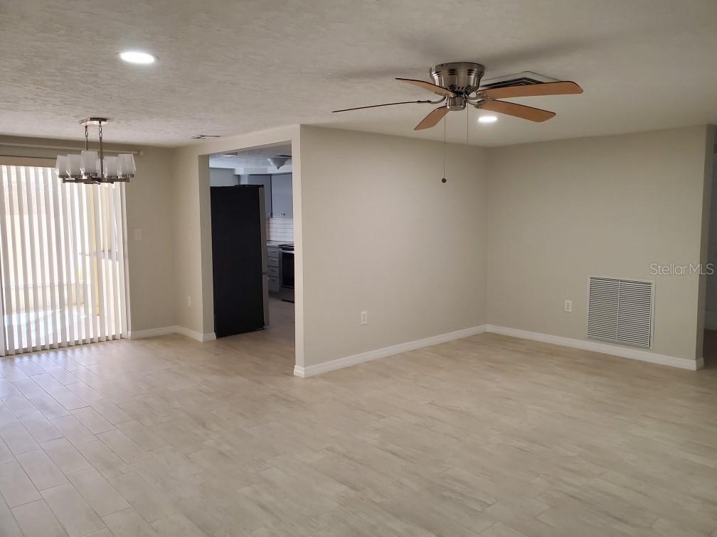 A living room with light-colored tile flooring, a ceiling fan, and an adjacent kitchen — 8504 WAGON WHEEL LANE, HUDSON, FL