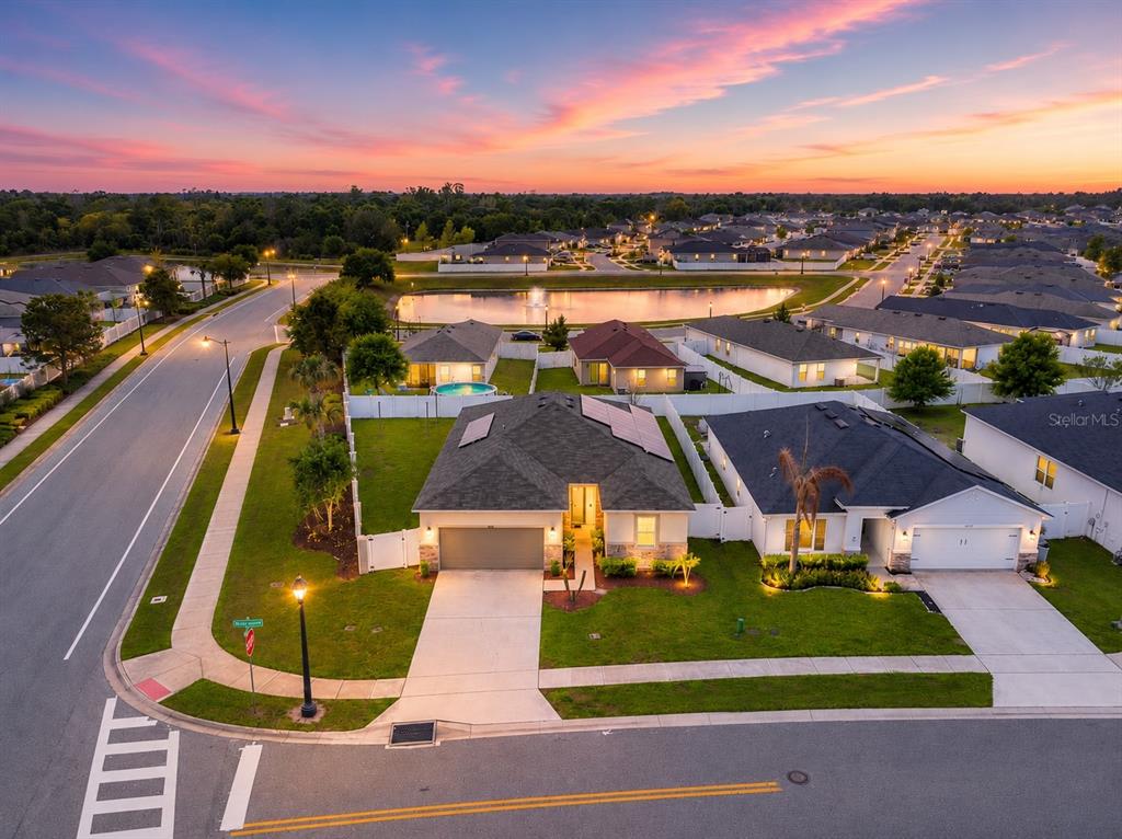 An aerial view of a suburban neighborhood featuring houses with solar panels and a pond — 4566 ORCHARD GROVE ROAD, ST CLOUD, FL