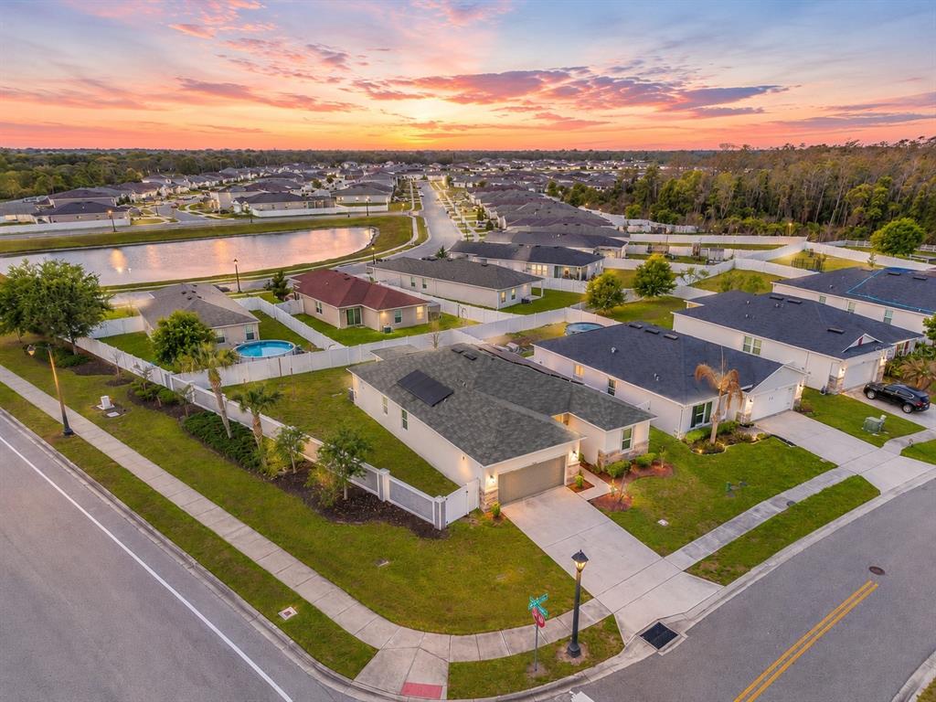 An aerial view shows a suburban neighborhood with houses, a pond, and sunset skies — 4566 ORCHARD GROVE ROAD, ST CLOUD, FL
