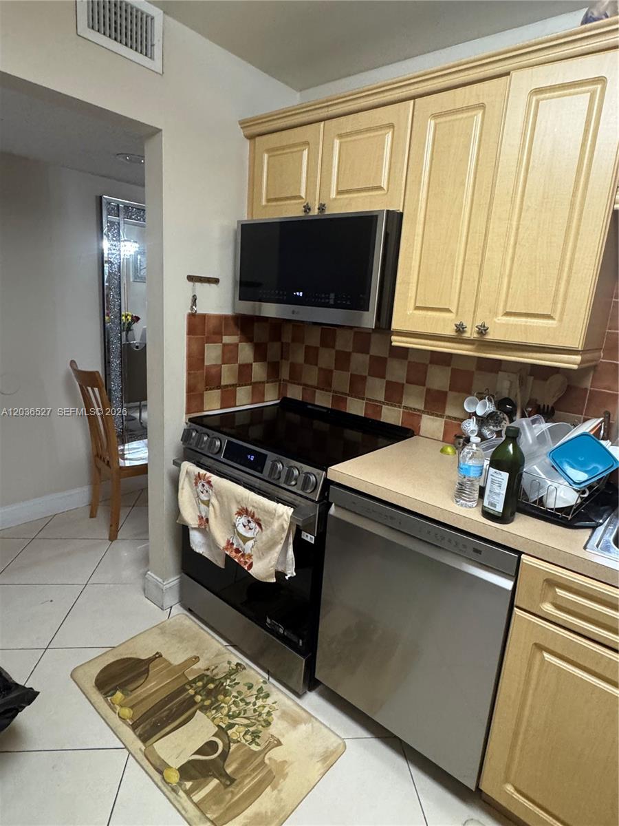 A kitchen features light wood cabinets, stainless steel appliances, and a checkered tile backsplash — 8625 NW 8th St # 310, Miami FL 33126, MIAMI, FL