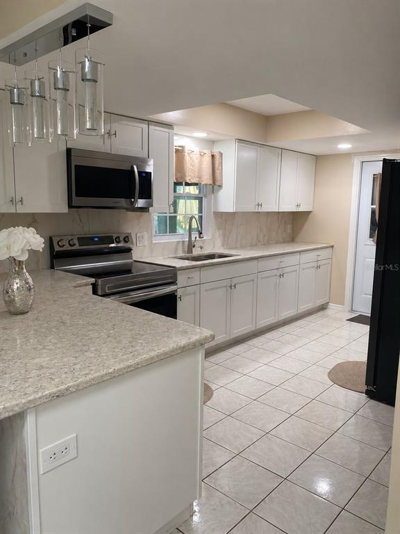 A kitchen features white cabinets, stainless steel appliances, light countertops, and a tiled floor — 4805 SPARROW DRIVE, ST CLOUD, FL