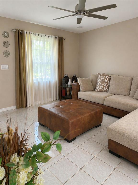 A living room features a beige sectional sofa, a large brown leather ottoman, and tile flooring — 4805 SPARROW DRIVE, ST CLOUD, FL
