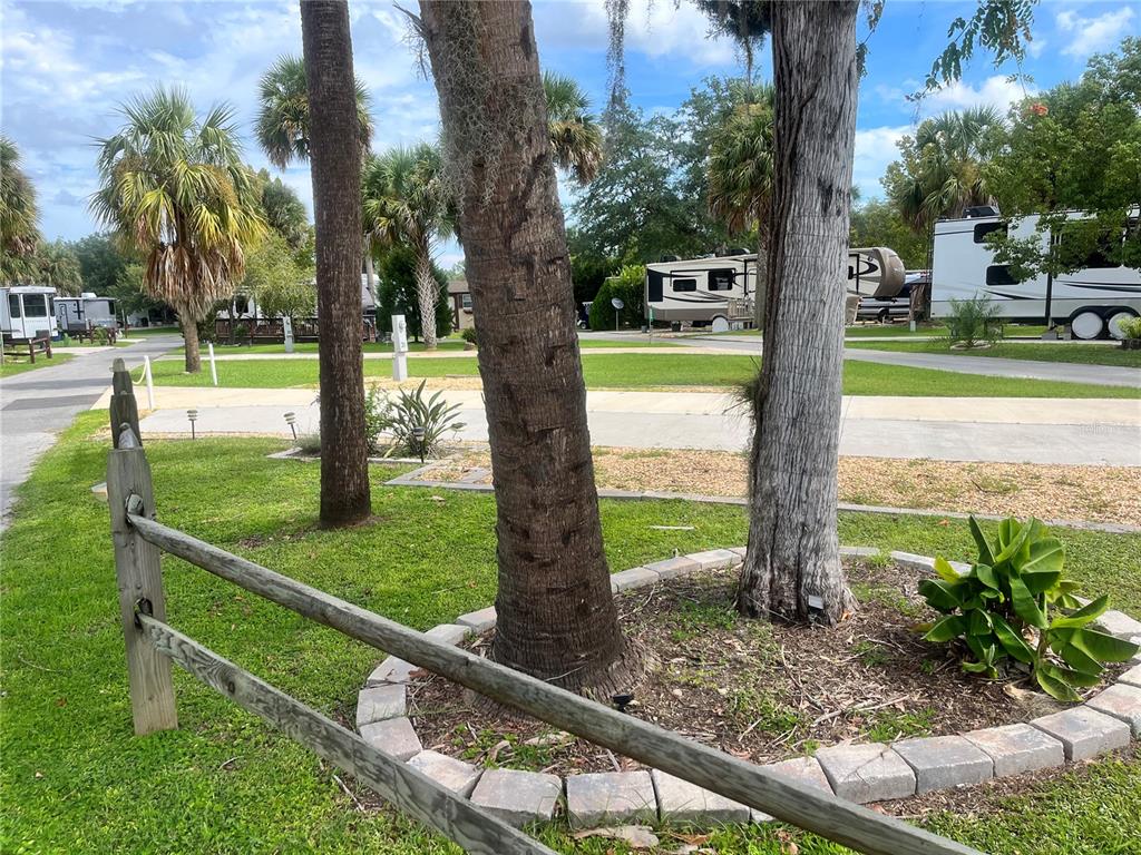 A wooden fence surrounds a landscaped tree bed in a grassy RV park setting — 2888 NE 102ND TERRACE, SILVER SPRINGS, FL