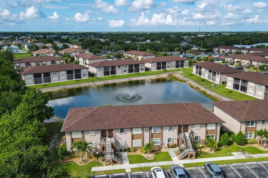 An aerial view of apartment buildings surrounding a central pond with a fountain — 25100 SANDHILL BOULEVARD UNIT J-201, PUNTA GORDA, FL