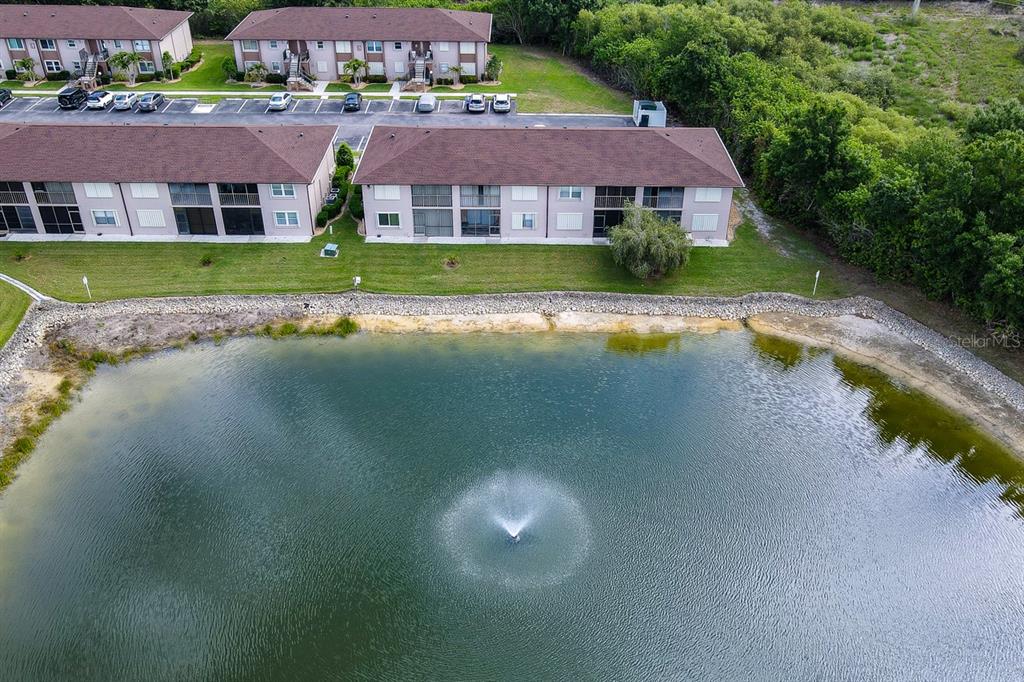 An aerial view shows apartment buildings situated next to a pond with a fountain — 25100 SANDHILL BOULEVARD UNIT J-201, PUNTA GORDA, FL