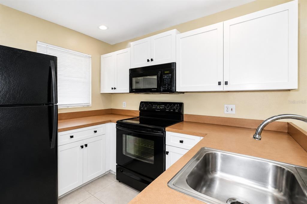 A kitchen features white cabinets, black appliances, tan countertops, and a stainless steel sink — 25100 SANDHILL BOULEVARD UNIT J-201, PUNTA GORDA, FL