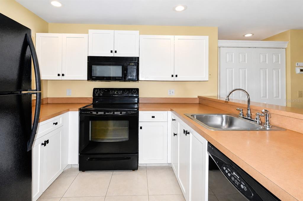 A kitchen with white cabinets, black appliances, tan countertops, and light-colored tile flooring — 25100 SANDHILL BOULEVARD UNIT J-201, PUNTA GORDA, FL