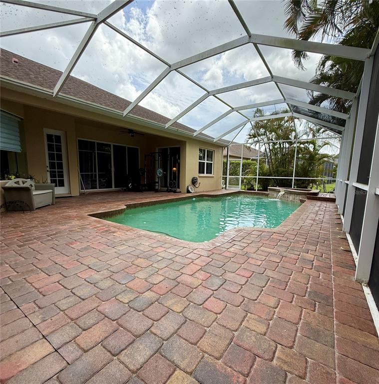 A screened-in patio features a swimming pool with a waterfall and brick paver decking — 11805 SOFT RUSH TERRACE, BRADENTON, FL