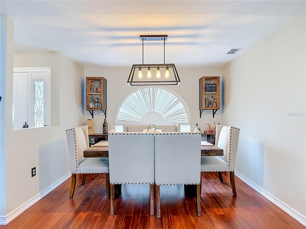 A dining room features a wooden table, upholstered chairs, a rectangular chandelier, and wall-mounted cabinets — 4539 MURCROSS LANE, NEW PORT RICHEY, FL