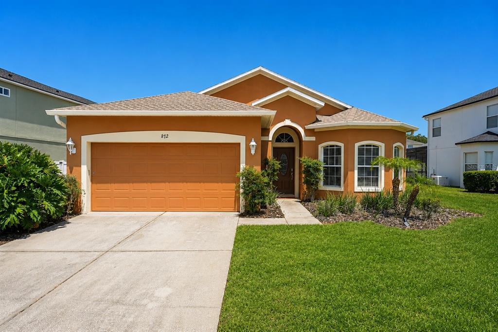A single-story house with an orange stucco exterior, a two-car garage, and a front lawn — 872 SUSSEX DRIVE, DAVENPORT, FL