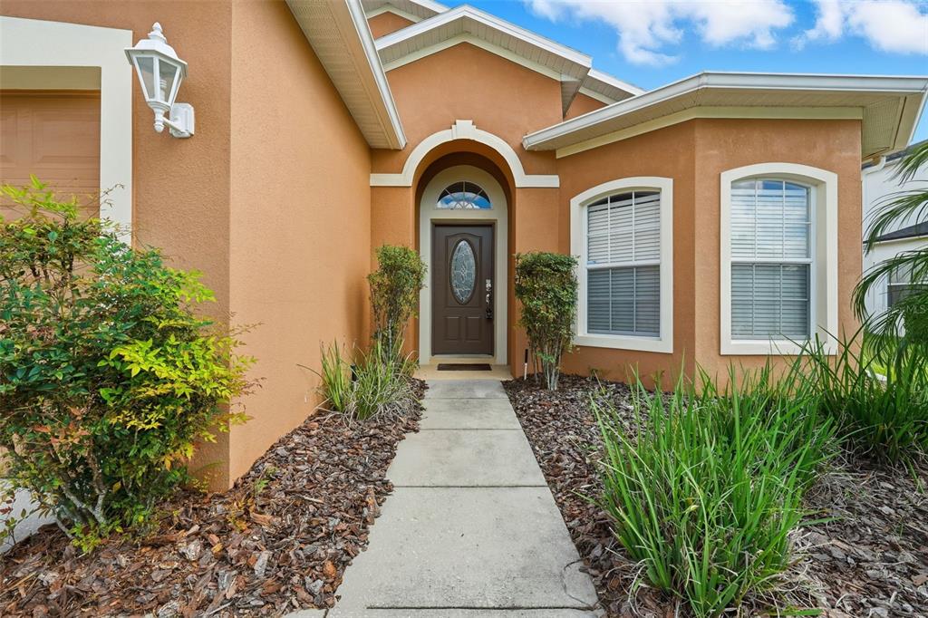 A concrete walkway leads to the front entrance of a tan stucco house — 872 SUSSEX DRIVE, DAVENPORT, FL