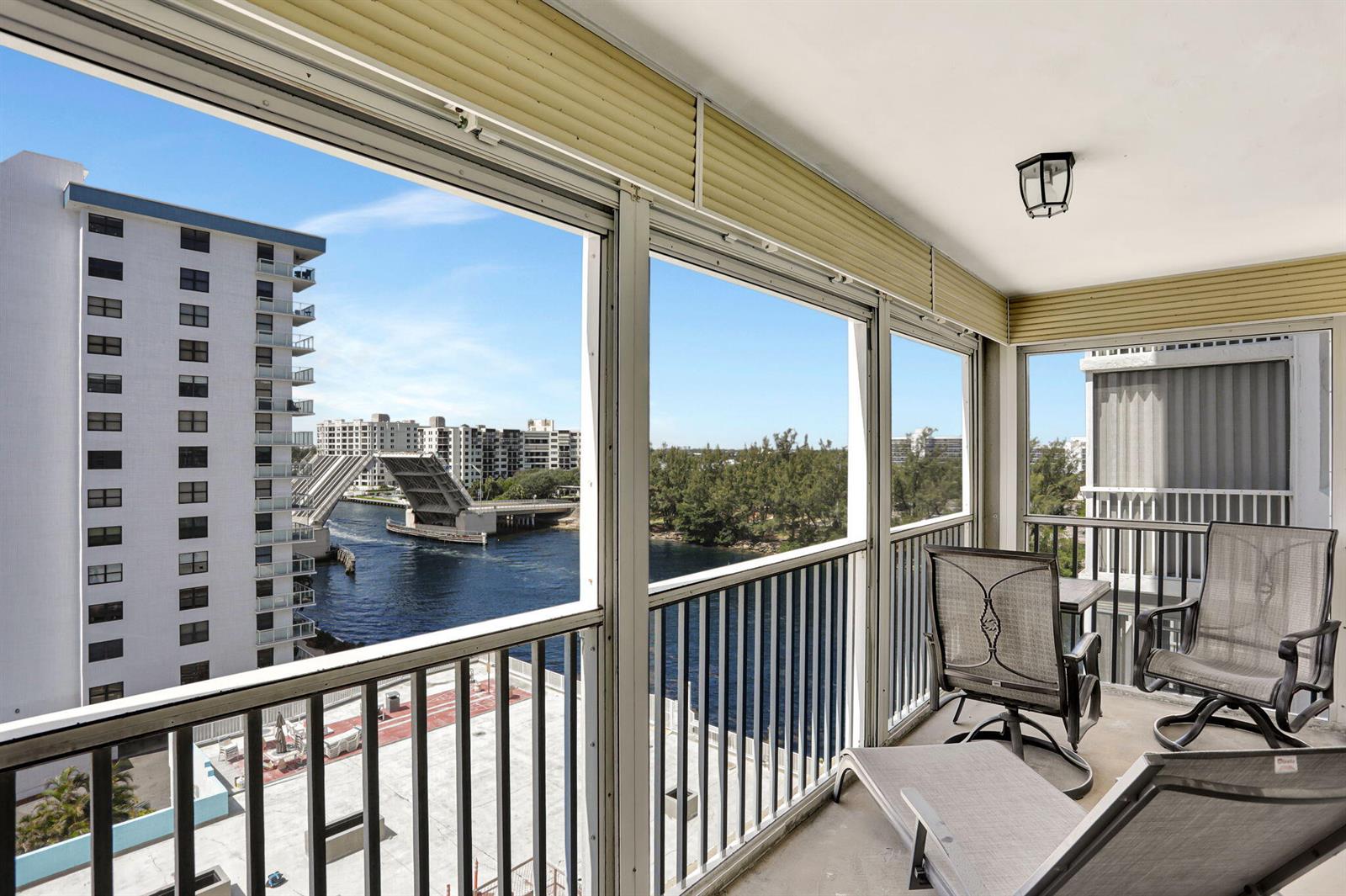 A balcony with outdoor furniture overlooks a waterway and a drawbridge between two buildings — 1505 N Riverside Drive # 802, Pompano Beach FL 33062, POMPANO BEACH, FL