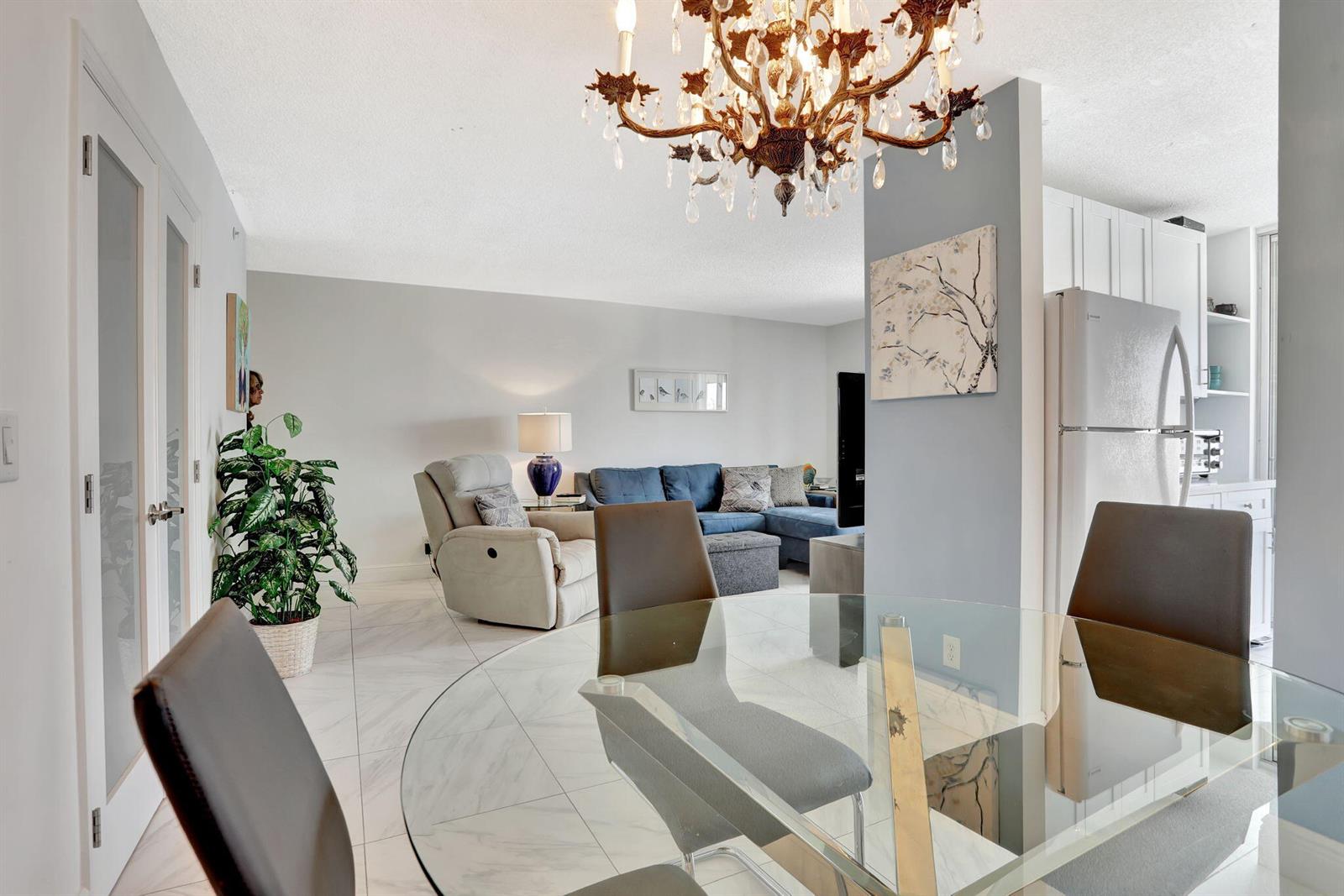 A dining area with a glass table overlooks a living room featuring a blue sofa — 1505 N Riverside Drive # 802, Pompano Beach FL 33062, POMPANO BEACH, FL