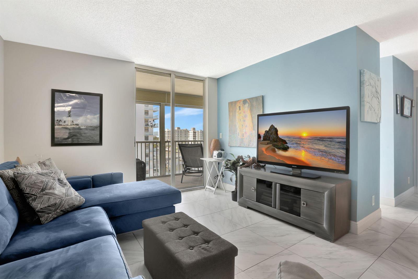 A living room features a blue sectional sofa, a television on a console, and a balcony — 1505 N Riverside Drive # 802, Pompano Beach FL 33062, POMPANO BEACH, FL
