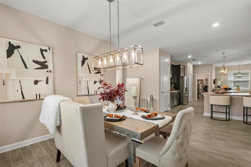 A dining room features a wooden table, upholstered chairs, a linear chandelier, and abstract art — 2537 CAMDEN PARK CIRCLE, DAVENPORT, FL