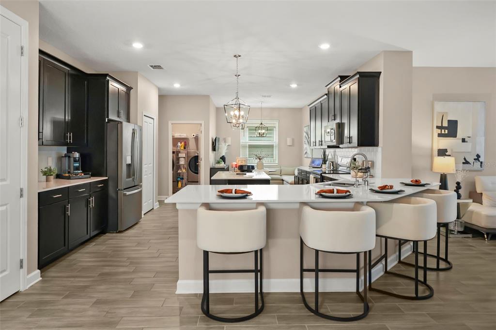 A modern kitchen features dark cabinets, white countertops, a breakfast bar, and light wood flooring — 2537 CAMDEN PARK CIRCLE, DAVENPORT, FL