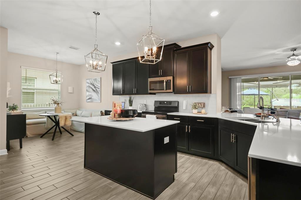 A modern kitchen features dark cabinetry, a white island, and light wood-look tile flooring — 2537 CAMDEN PARK CIRCLE, DAVENPORT, FL