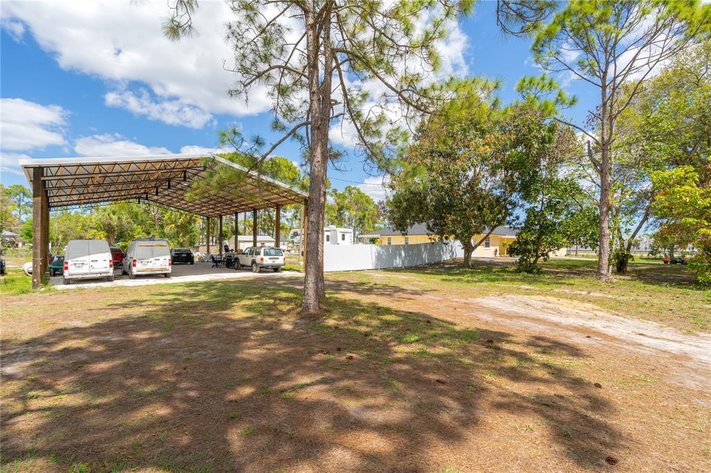 A large metal carport stands on a grassy lot with several vehicles parked underneath — 17075 ORANGE GROVE BOULEVARD, LOXAHATCHEE, FL
