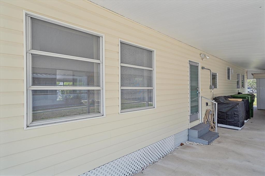 A side view of a mobile home exterior featuring light siding, windows, and a carport — 1100 UNIVERSITY PARKWAY UNIT 58, SARASOTA, FL