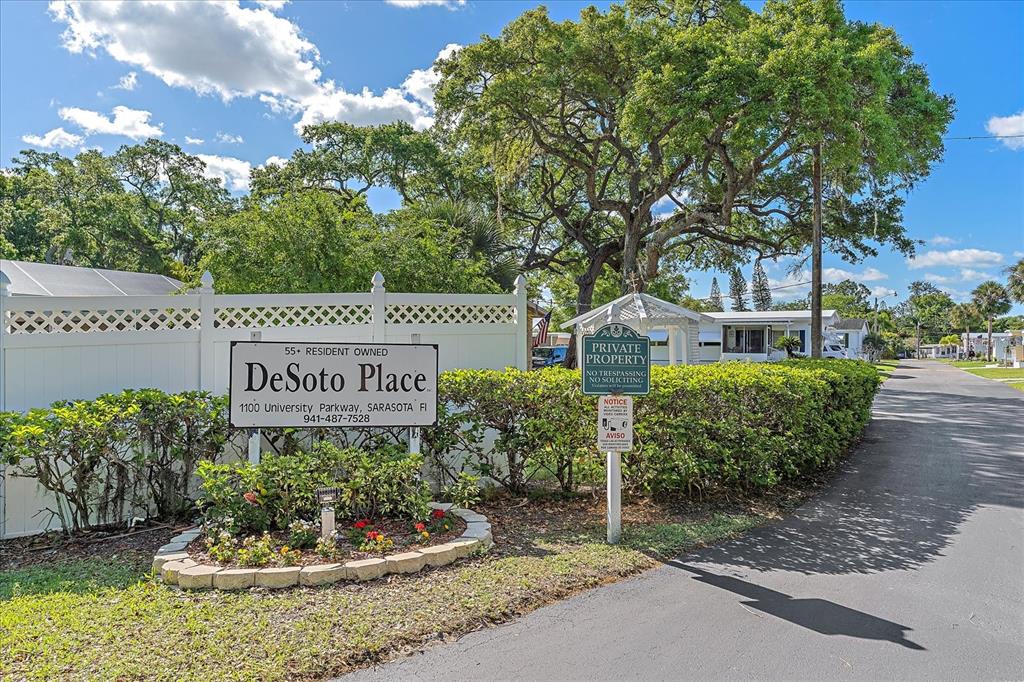 A sign for DeSoto Place stands in front of a white fence and large trees — 1100 UNIVERSITY PARKWAY UNIT 58, SARASOTA, FL