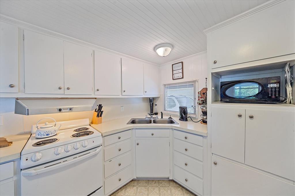 A white kitchen features a corner sink, electric range, and built-in microwave cabinet — 1100 UNIVERSITY PARKWAY UNIT 58, SARASOTA, FL