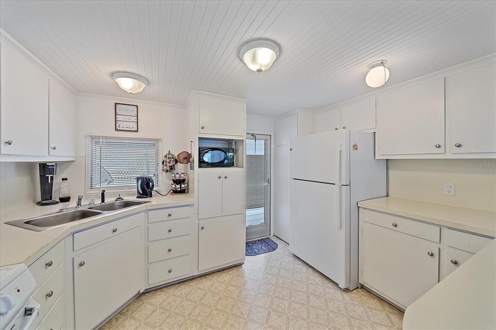 A white kitchen features laminate countertops, white cabinetry, a double sink, and a refrigerator — 1100 UNIVERSITY PARKWAY UNIT 58, SARASOTA, FL