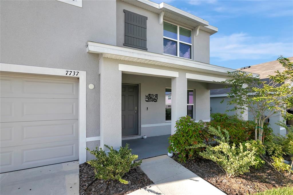 A two-story house exterior features a gray stucco facade, a garage, and a covered entryway — 7737 ROSEWOOD GARDEN LOOP, TAMPA, FL