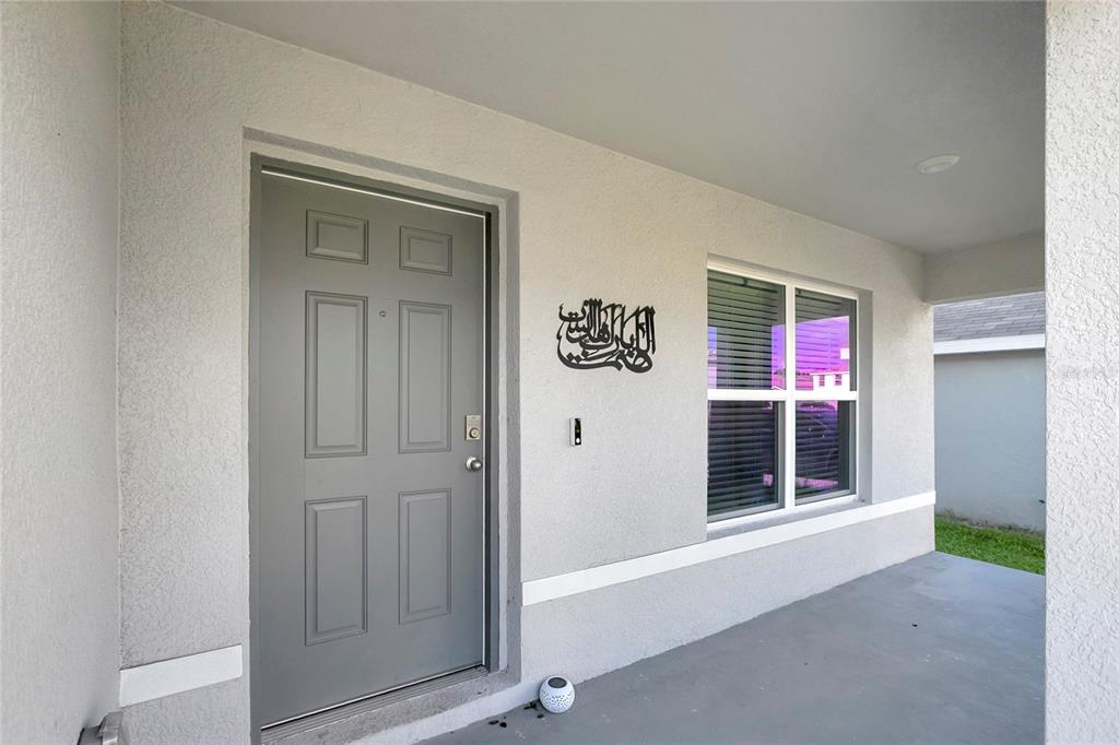 A gray front door and a window are on the exterior porch of a house — 7737 ROSEWOOD GARDEN LOOP, TAMPA, FL