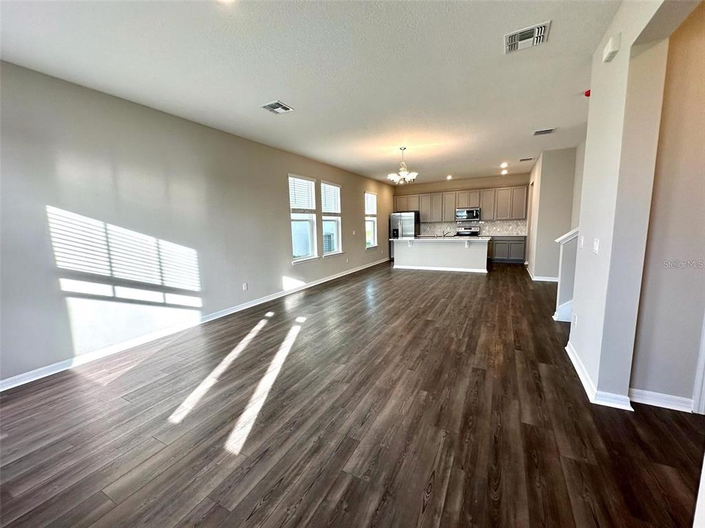 An open-concept living and kitchen area features dark wood-look flooring and light gray walls — 4869 LACEWING DRIVE, WINTER GARDEN, FL